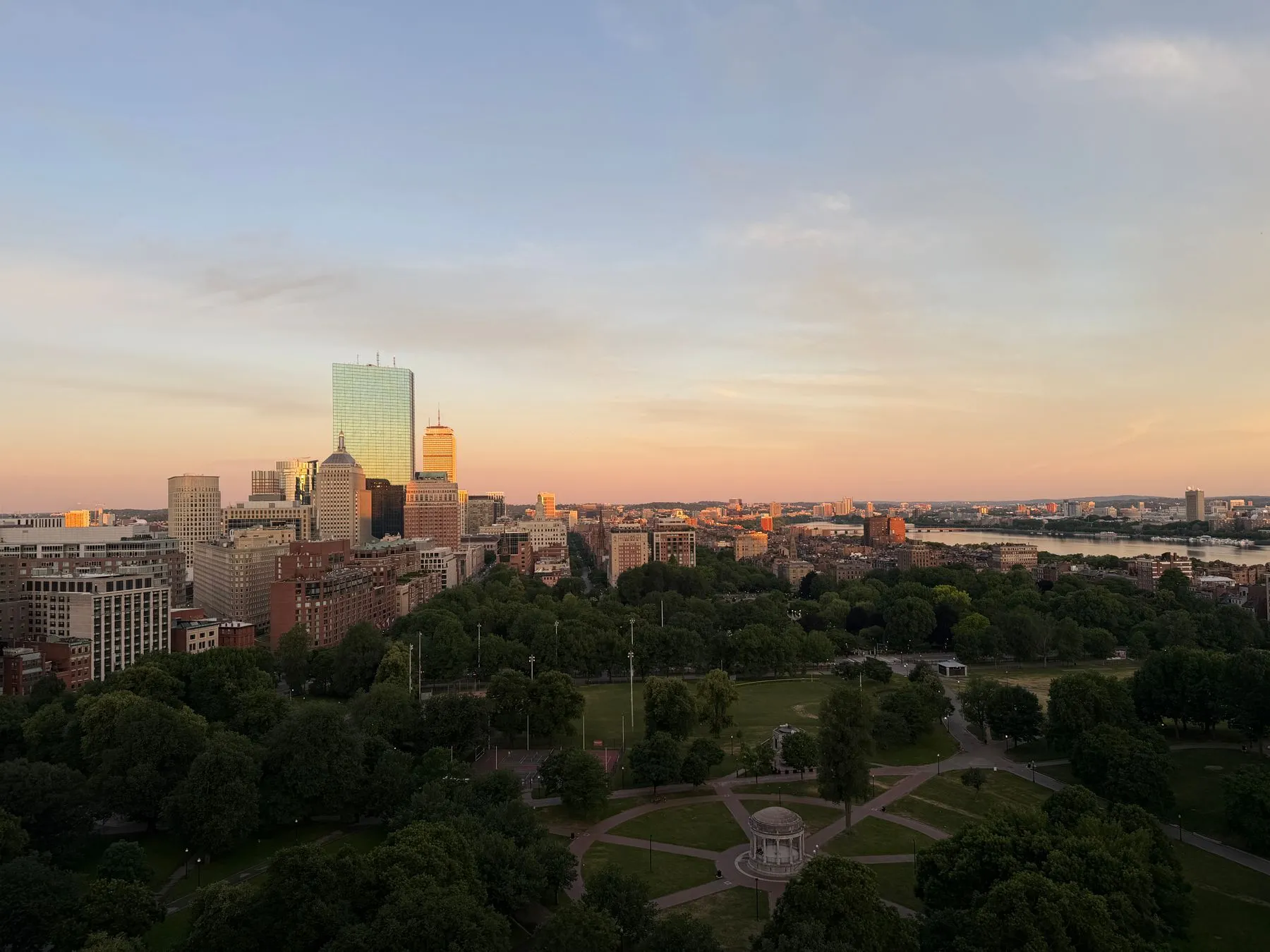 Boston Public Garden at sunset with the city skyline behind it — the B.A.A. buses load on Charles Street between here and Boston Common.